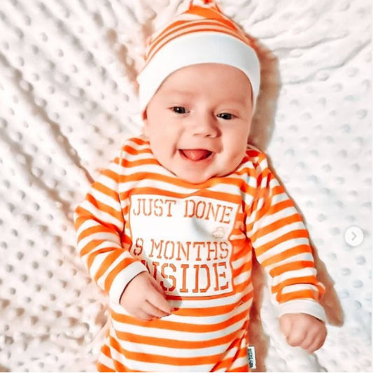 Baby wearing orange and white striped Just Done 9 Months Inside baby grow with matching hat