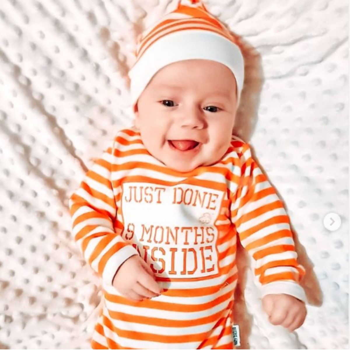 Baby wearing orange and white striped Just Done 9 Months Inside baby grow with matching hat
