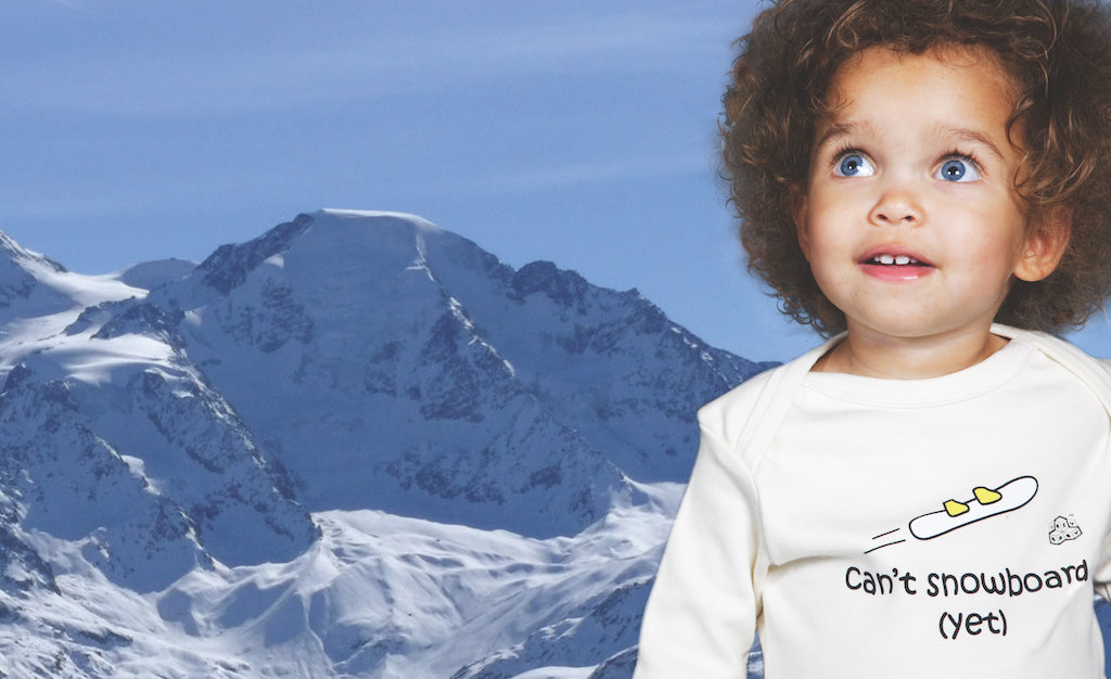 Baby wearing can't snowboard t shirt with snowy mountains in background